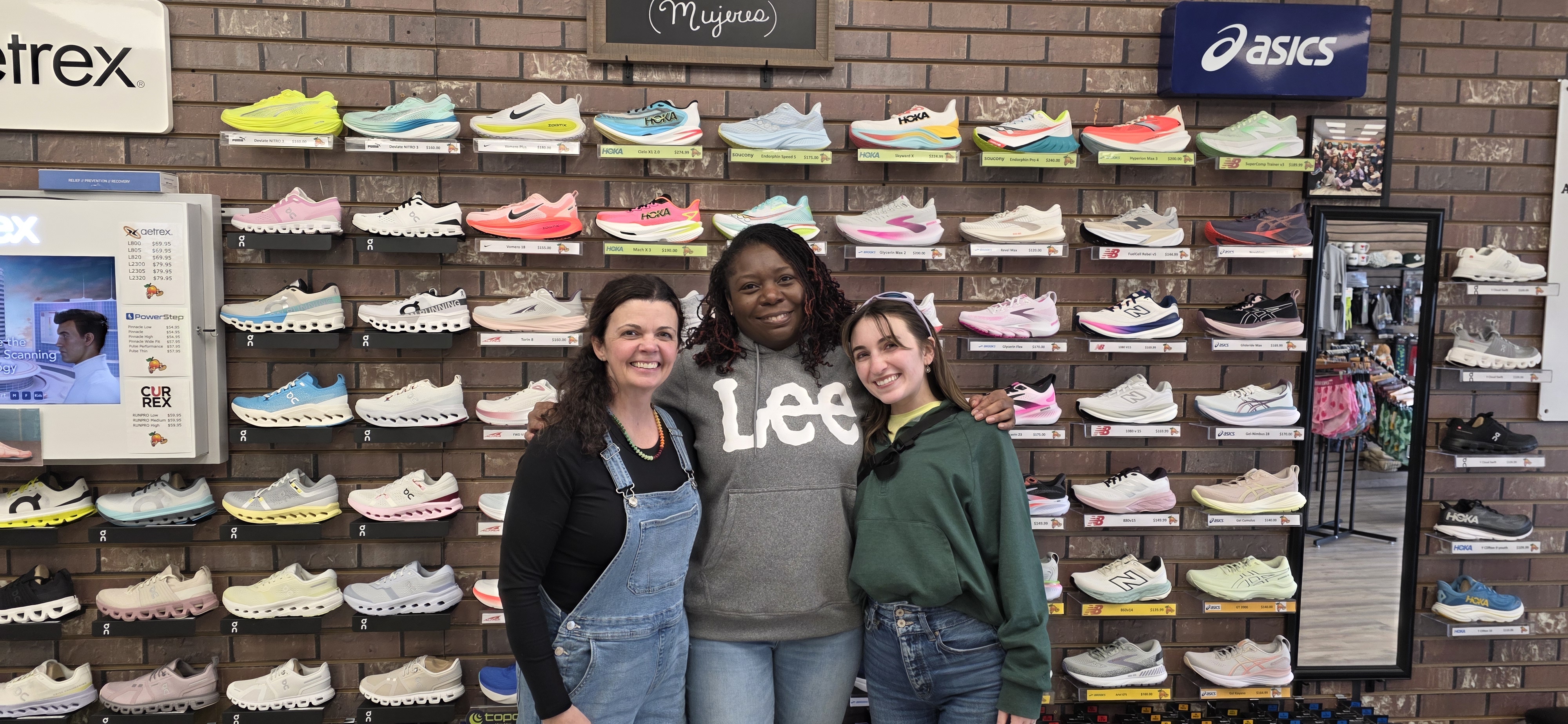 Three women standing in front of a wall of shoes inside Big Peach Running Company